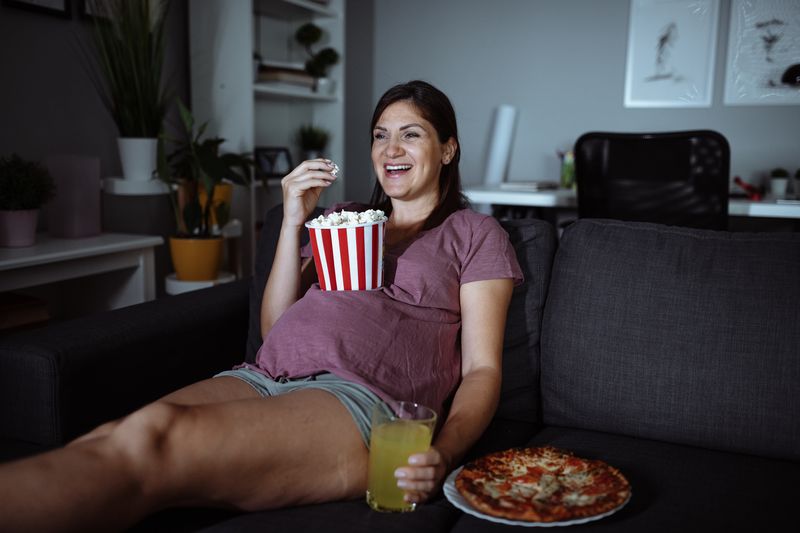 Eine schwangere Frau isst Popcorn, während sie sich einen Film ansieht.