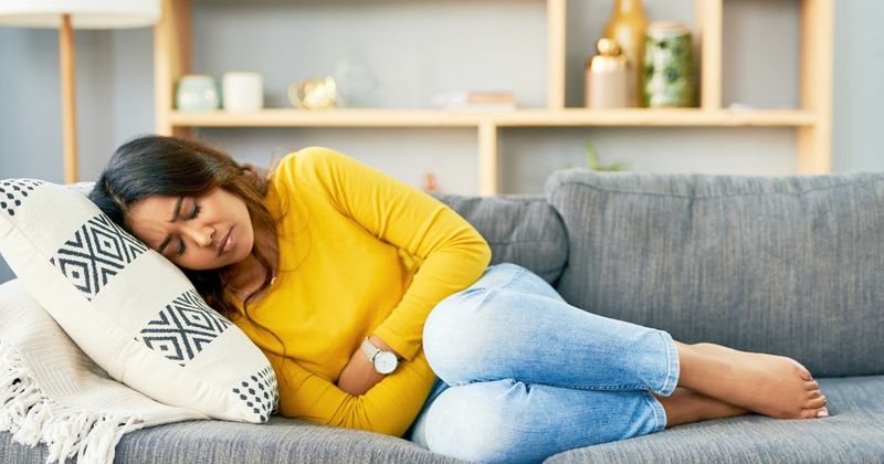 Frau, die sich an den Bauch klammert – Positionen, die gegen Periodenkrämpfe helfen