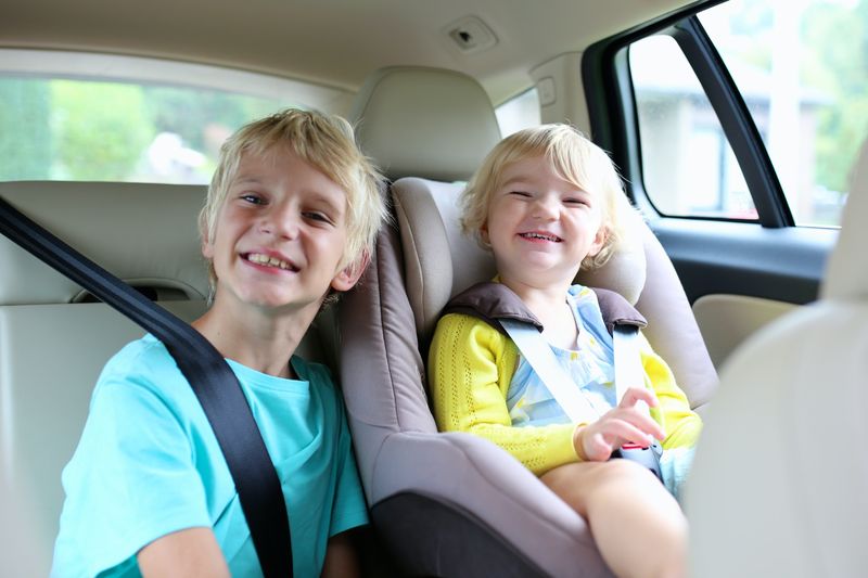 Glückliche Kinder, entzückendes Kleinkindmädchen mit Teenagerbruder, die zusammen in modernem Auto sitzen, das mit ...