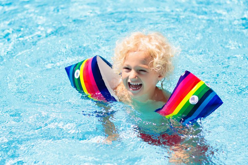 Kind im Schwimmbad mit bunten aufblasbaren Armbinden. Kinder lernen mit Schwimmhilfen schwimmen. Flo...