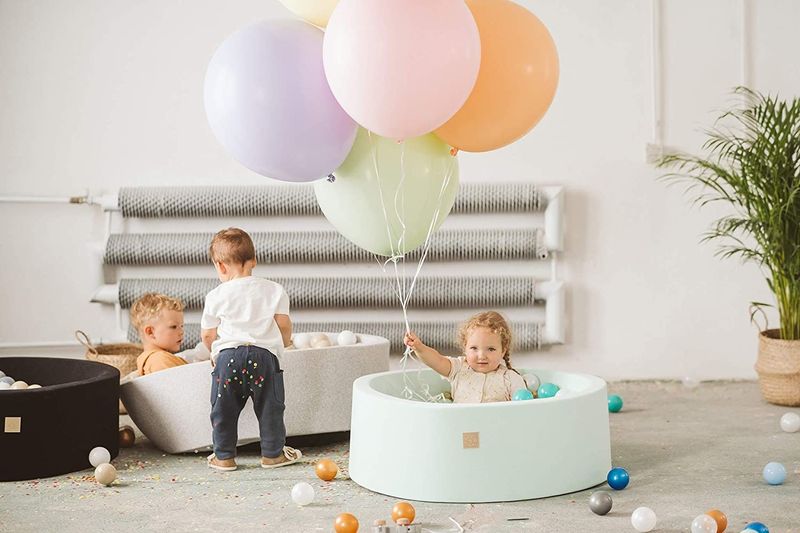 Drei Kleinkinder, die mit Kugelgruben und Ballonen spielen