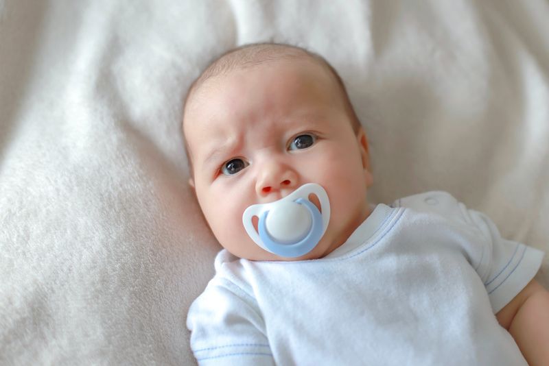 Headshot-Porträt eines süßen Neugeborenen, das mit Schnuller auf dem Mund auf dem Bett liegt. Gemischte Abstammung asiatisch-deutsch ...