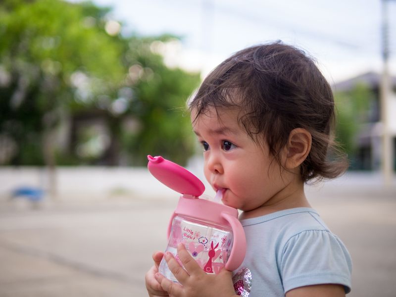 Close-up Babymädchen trinken Wasser aus der Flasche über Strohhalm, während sie im Freien spazieren gehen.