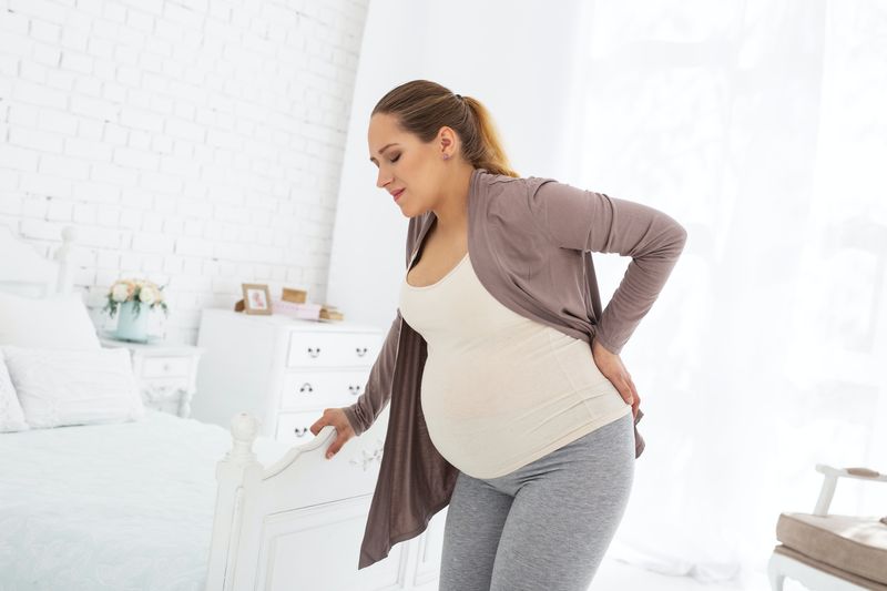 Beschwerden während der Schwangerschaft. Wütende schwangere Frau bleibt und berührt ihren Rücken